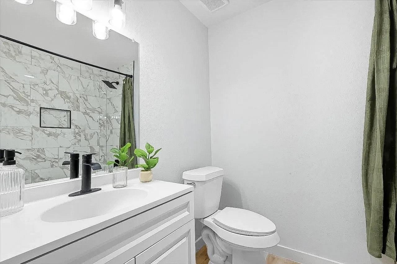 Guest bathroom with white vanity, black fixtures, marble-look tub surround, and green shower curtain in Lewisville.
