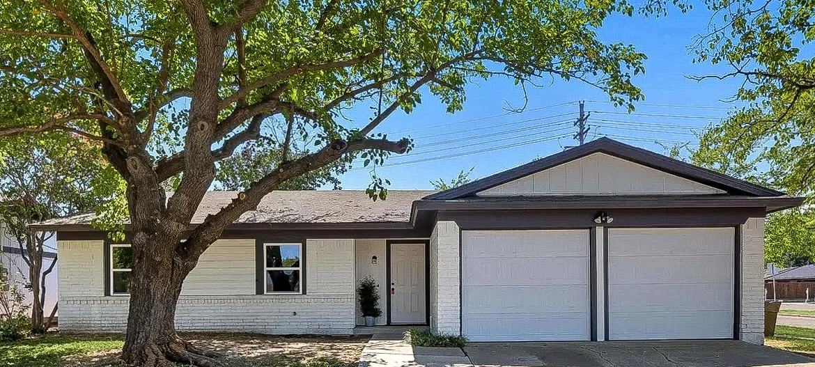 Brick home with fresh light exterior paint, dark roof, black windows, and two-car garage in Lewisville.