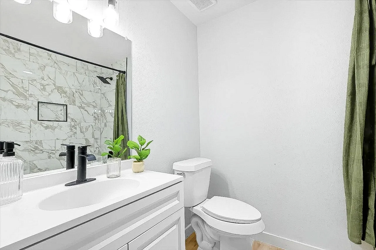 Guest bathroom with a marble-look tub surround, white vanity, black fixtures, and a bright neutral finish in Lewisville, Texas.