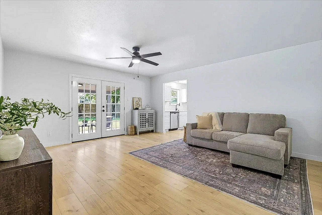 Living room with new light wood flooring, white walls, ceiling fan, French doors, and staged seating in Lewisville, Texas.