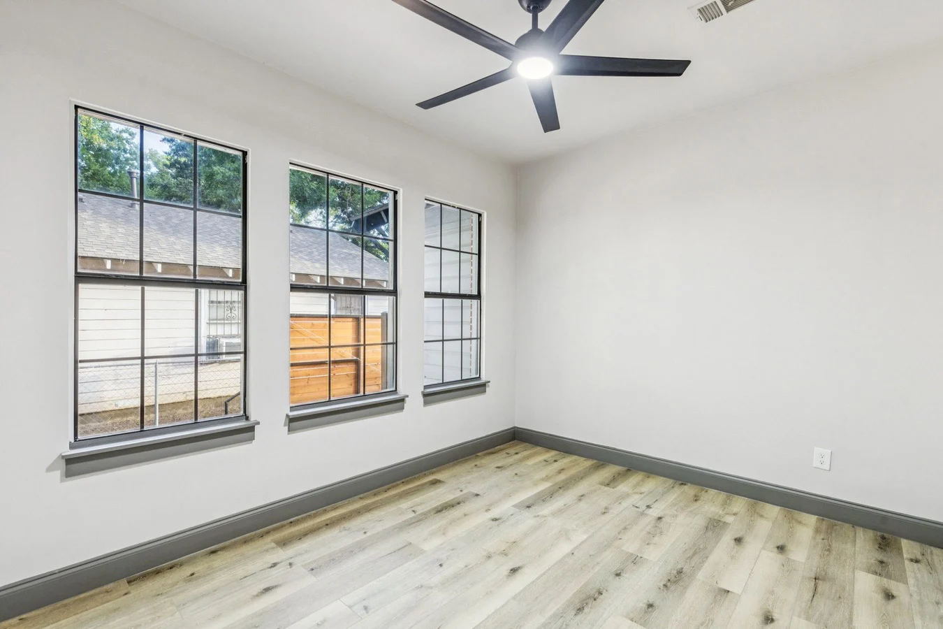 Secondary bedroom with black-framed windows, light wood-look flooring, white walls, gray trim, and ceiling fan in Lewisville, Texas.