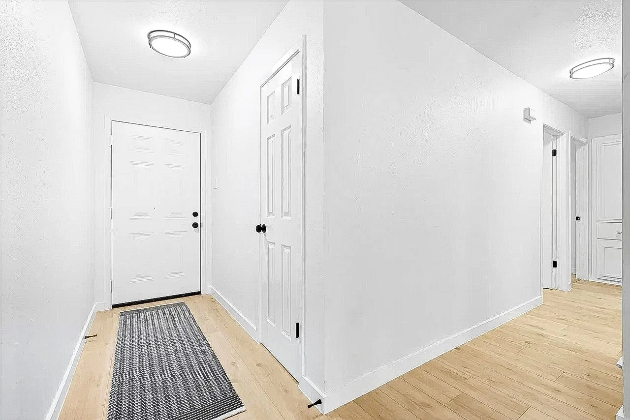 Bright remodeled hallway and entry circulation with light wood flooring, white walls, black hardware, and clean trim in Lewisville, Texas.