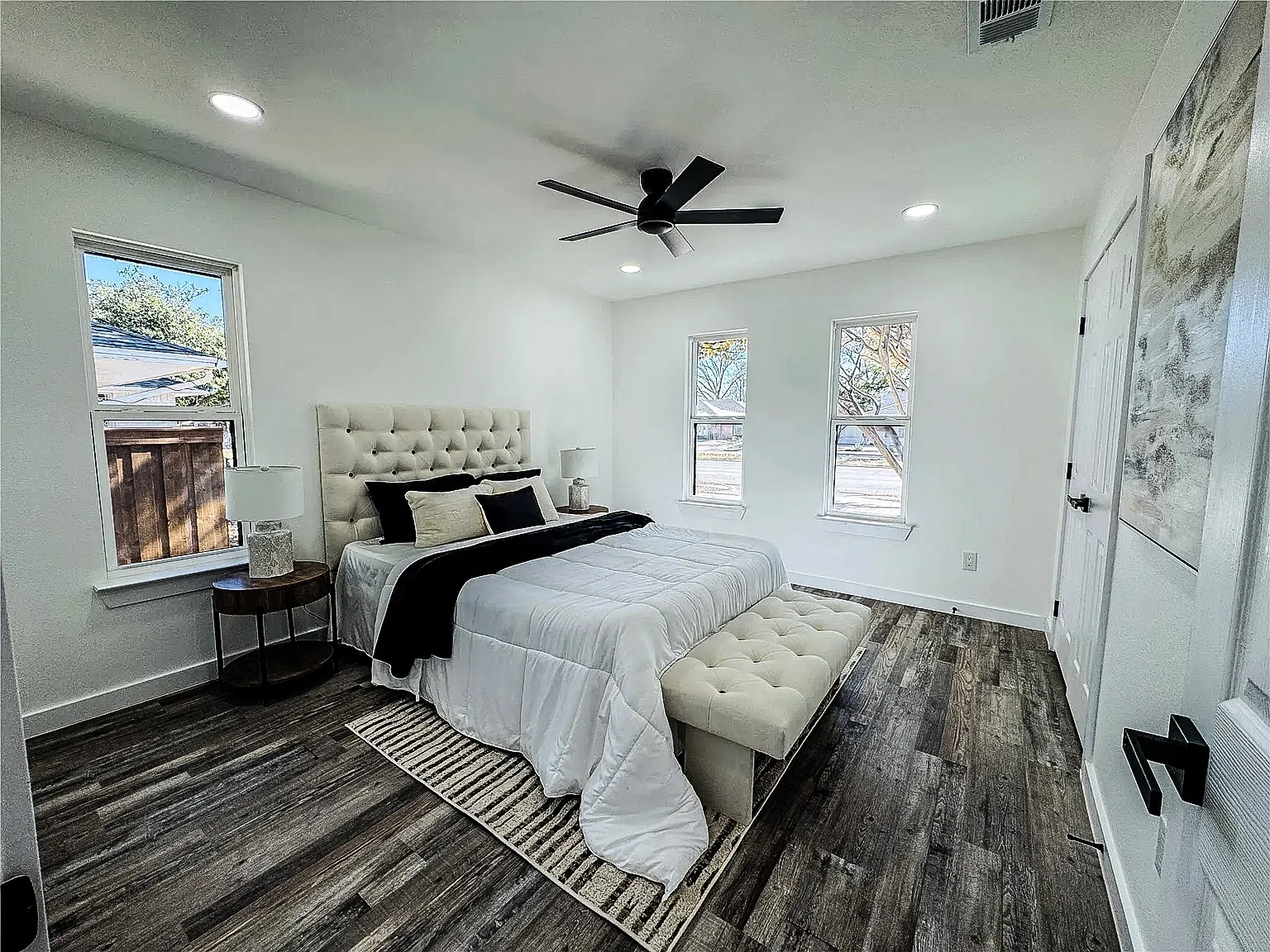 Bedroom with new wood-look flooring, white walls, black windows, and ceiling fan in Lower Greenville, Dallas.