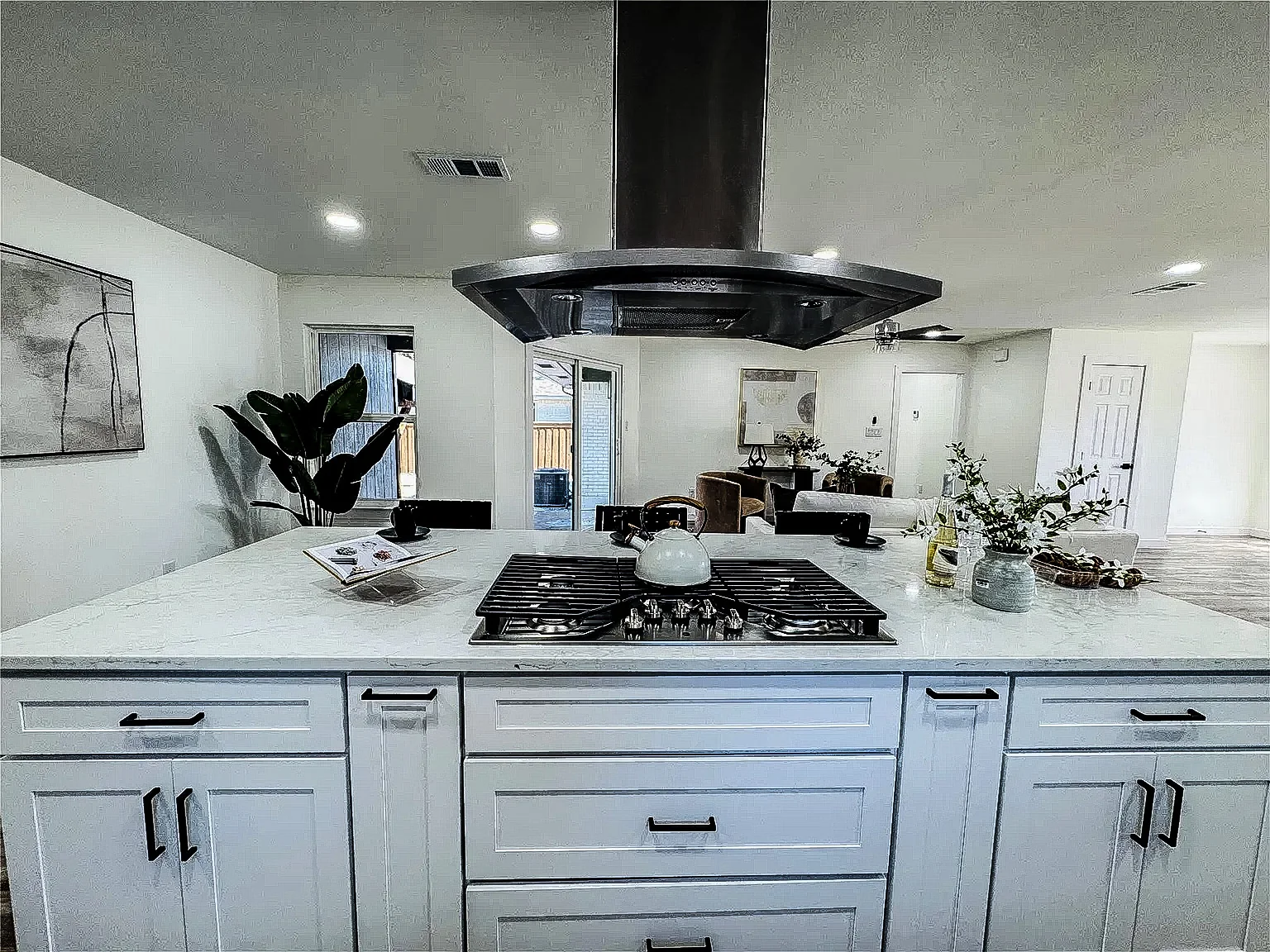 Kitchen island with white cabinetry, dark range hood, quartz surface, and open living space in Lower Greenville, Dallas.