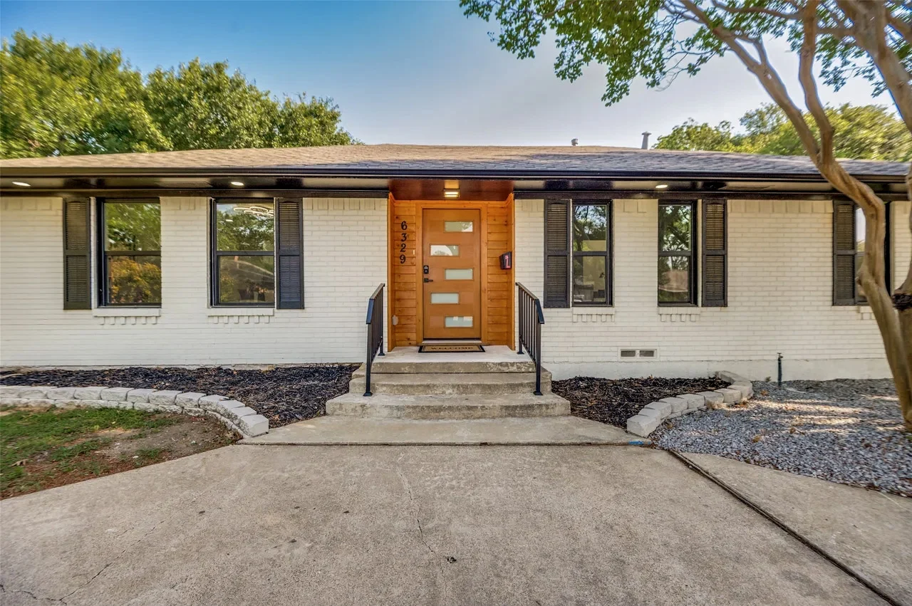 White brick Lower Greenville home with black replacement windows, modern wood entry door, and refreshed front landscaping in Lower Greenville, Dallas, Texas.