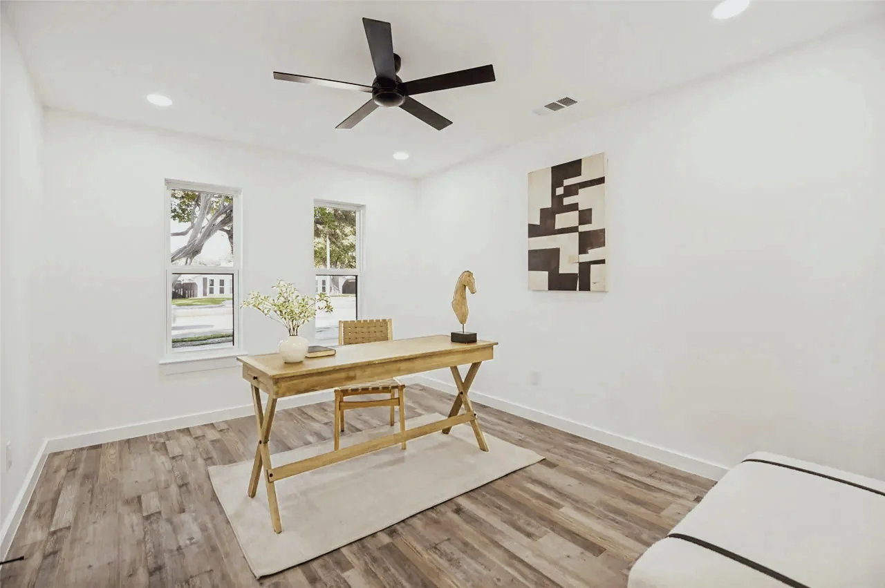 Bright home office with white walls, wood-look flooring, black ceiling fan, corner windows, and a staged desk area in Lower Greenville, Dallas, Texas.