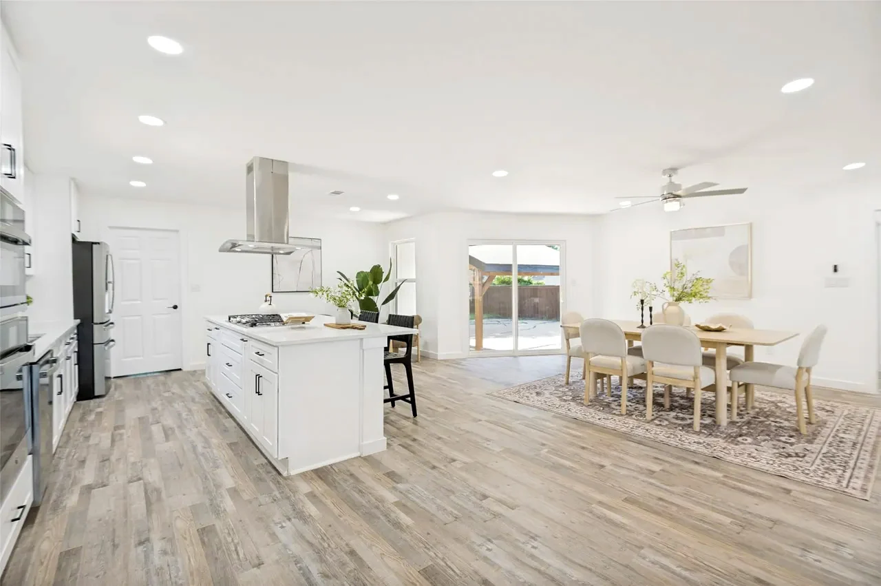 Open kitchen, dining, and living area with white cabinetry, a large island, light wood-look flooring, and bright white walls in Lower Greenville, Dallas, Texas.