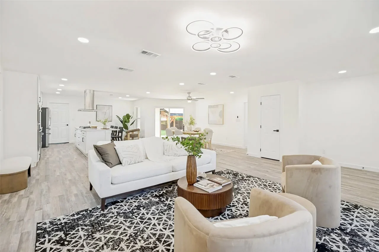 Wide living room view connected to the white kitchen and dining area with light wood-look flooring and staged furnishings in Lower Greenville, Dallas, Texas.