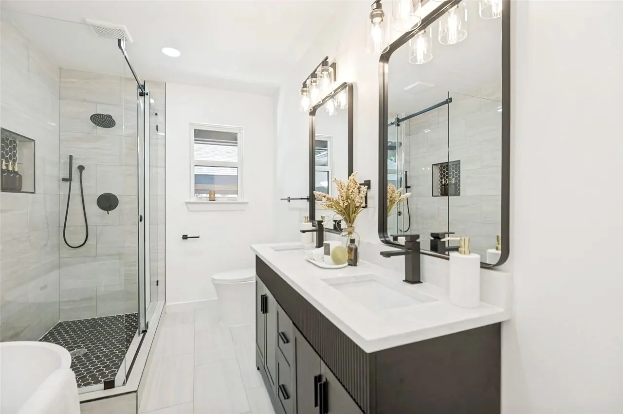 Primary bathroom with a glass wet room, rain shower, dark double vanity, white counters, and black fixtures in Lower Greenville, Dallas, Texas.