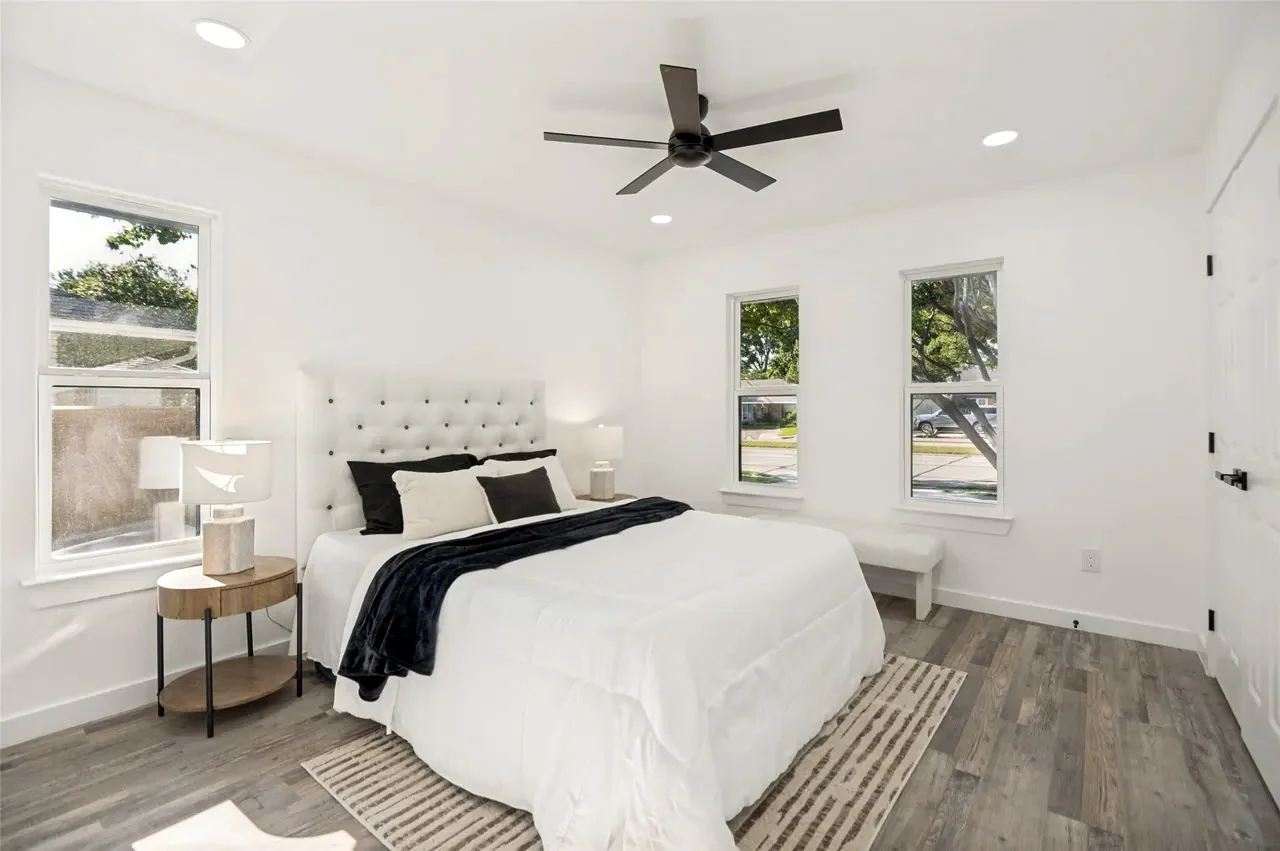 Secondary bedroom with white walls, wood-look flooring, black ceiling fan, three windows, and staged furnishings in Lower Greenville, Dallas, Texas.