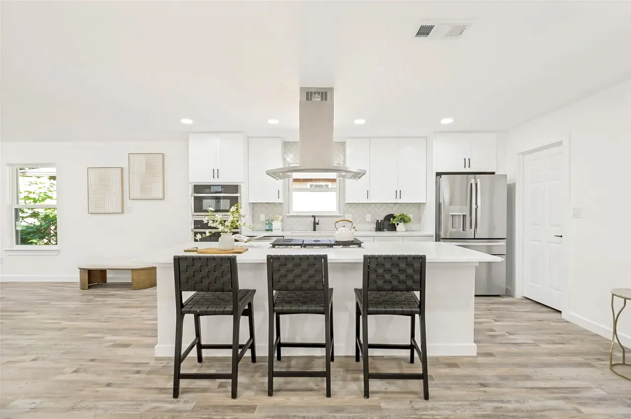 Large white kitchen island with black seating, waterfall-style ends, pendant lighting, and adjoining dining space in Lower Greenville, Dallas, Texas.