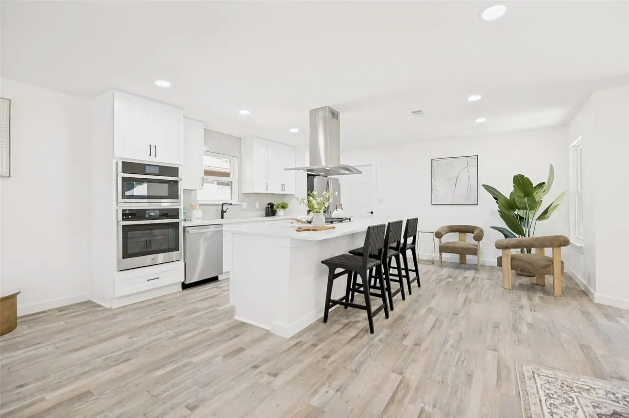 Open white kitchen and dining area with stainless appliances, a center island, recessed lighting, and light wood-look flooring in Lower Greenville, Dallas, Texas.