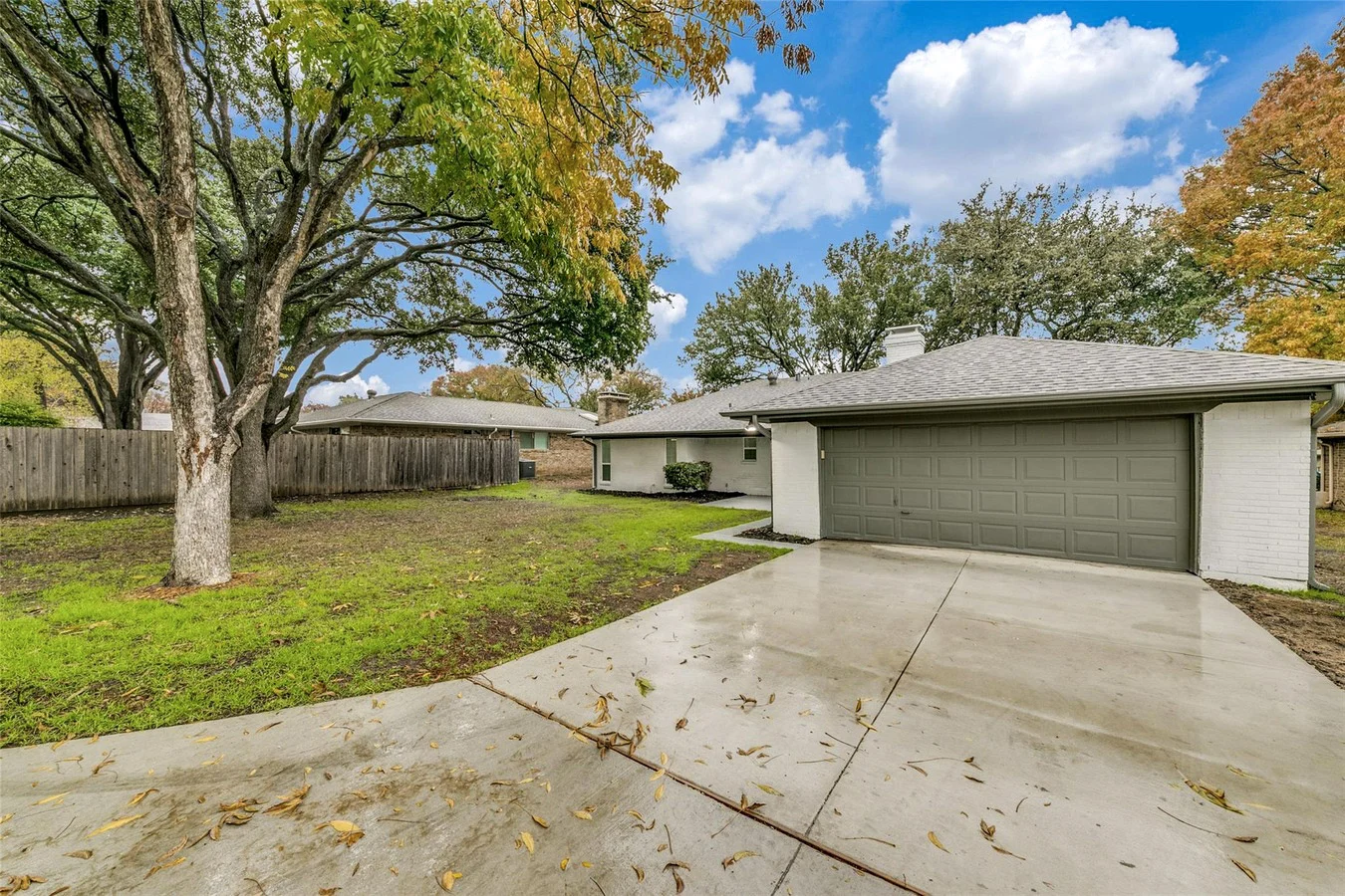 Fresh concrete driveway leading to a single-story Plano home with painted exterior, mature trees, and a two-car garage in Plano, Texas.