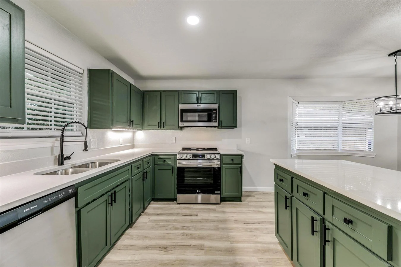 Deep green shaker kitchen with a large white island, stainless steel appliances, black fixtures, and light wood-look flooring in Plano, Texas.