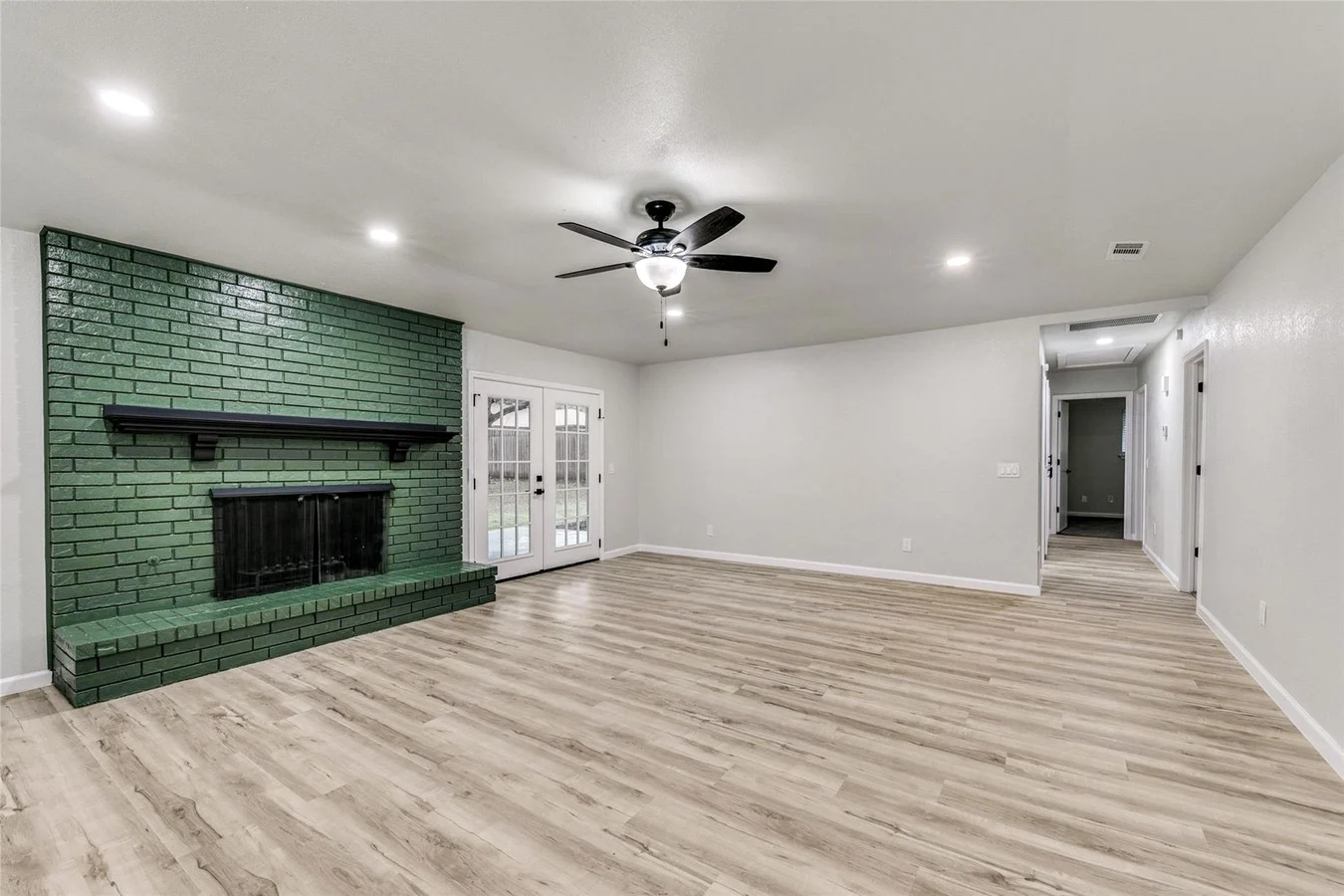 Living room with light wood-look flooring, a deep green painted fireplace, recessed lighting, and open circulation in Plano, Texas.