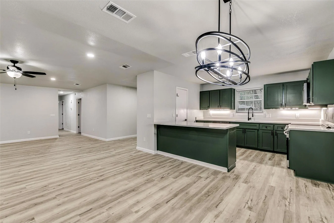 Open kitchen and living area after structural wall removal with a green island, recessed lighting, and light wood-look flooring in Plano, Texas.