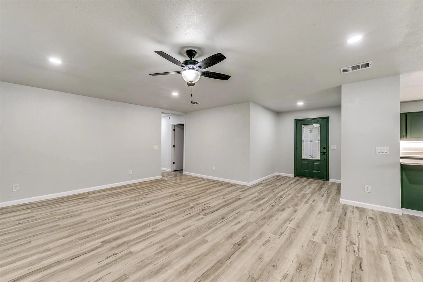 Open living area with fresh neutral paint, light wood-look flooring, recessed lighting, and a deep green front door in Plano, Texas.