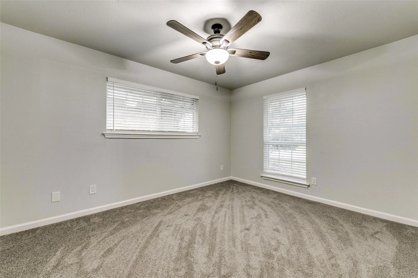 Corner secondary bedroom with new gray carpet, light gray walls, two windows, white trim, and ceiling fan in Plano, Texas.