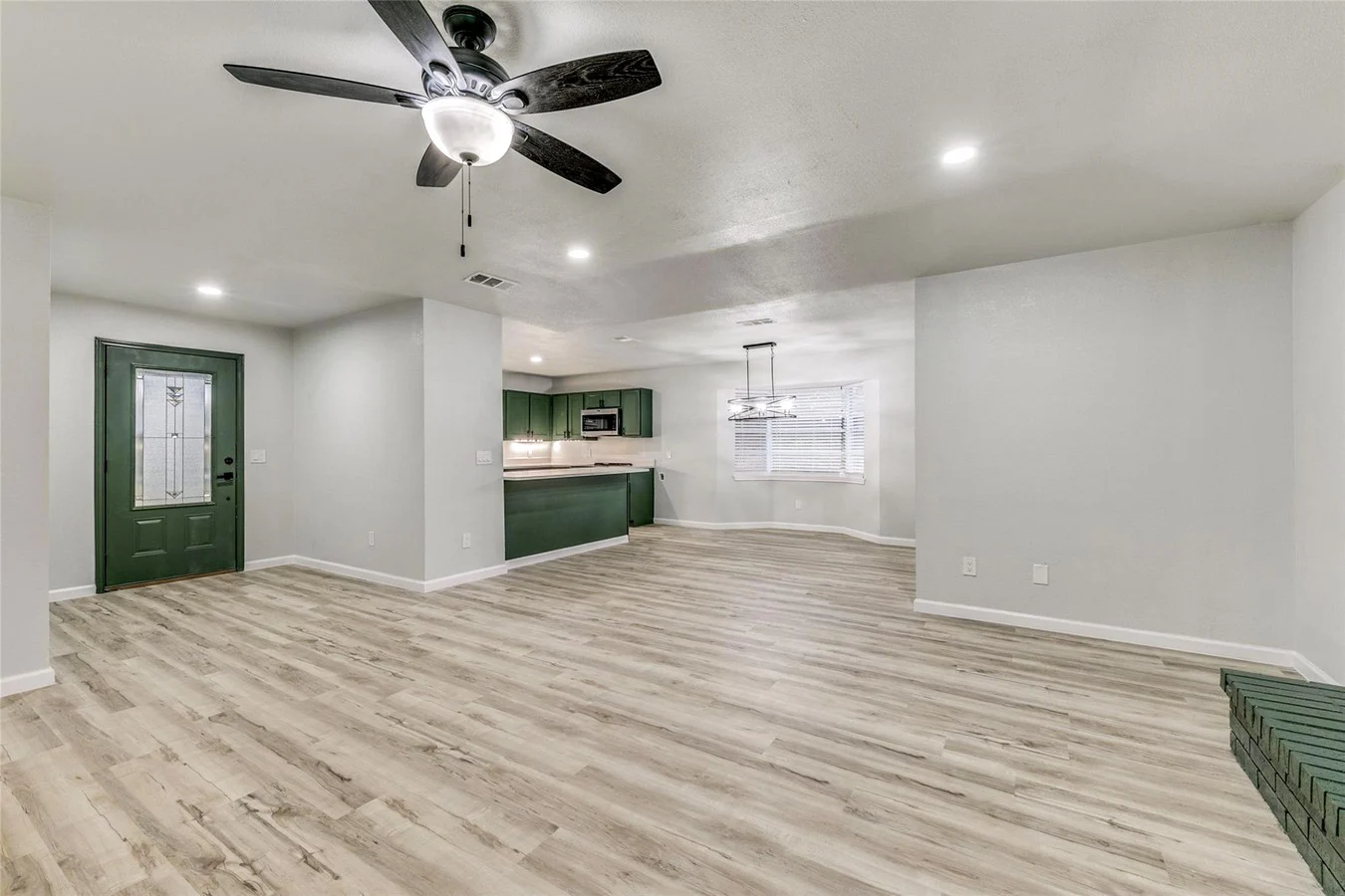 Whole-home view connecting the open living area to the deep green kitchen with light wood-look flooring and recessed lighting in Plano, Texas.