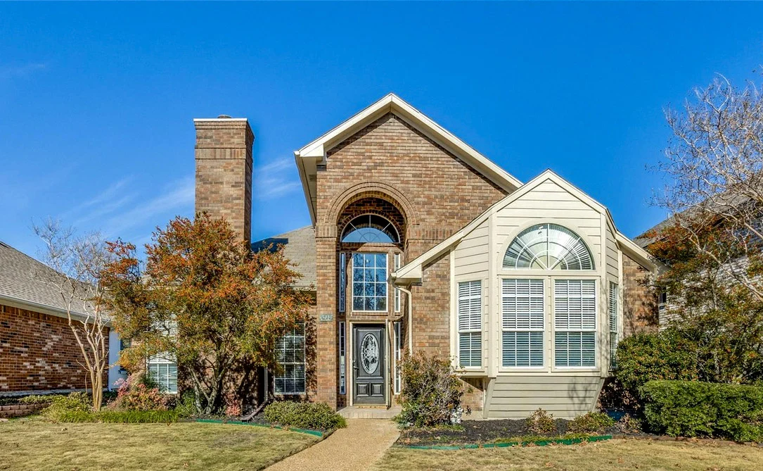 Two-story Rowlett brick exterior with arched windows, tall entry glazing, mature landscaping, and refreshed paint details in Rowlett, Texas.