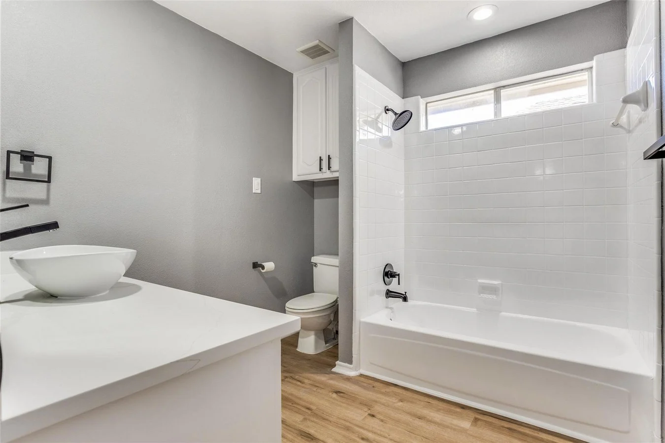 Guest bathroom with a white tub and shower, gray walls, white vanity, vessel sink, and black hardware in Rowlett, Texas.