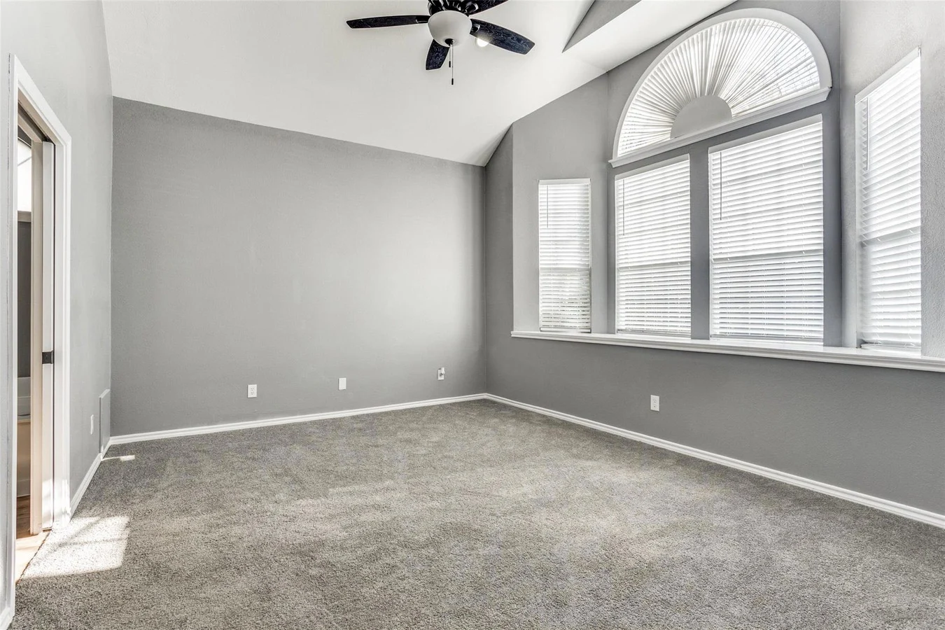Primary bedroom with gray carpet, gray walls, tall arched windows, white trim, and ceiling fan in Rowlett, Texas.