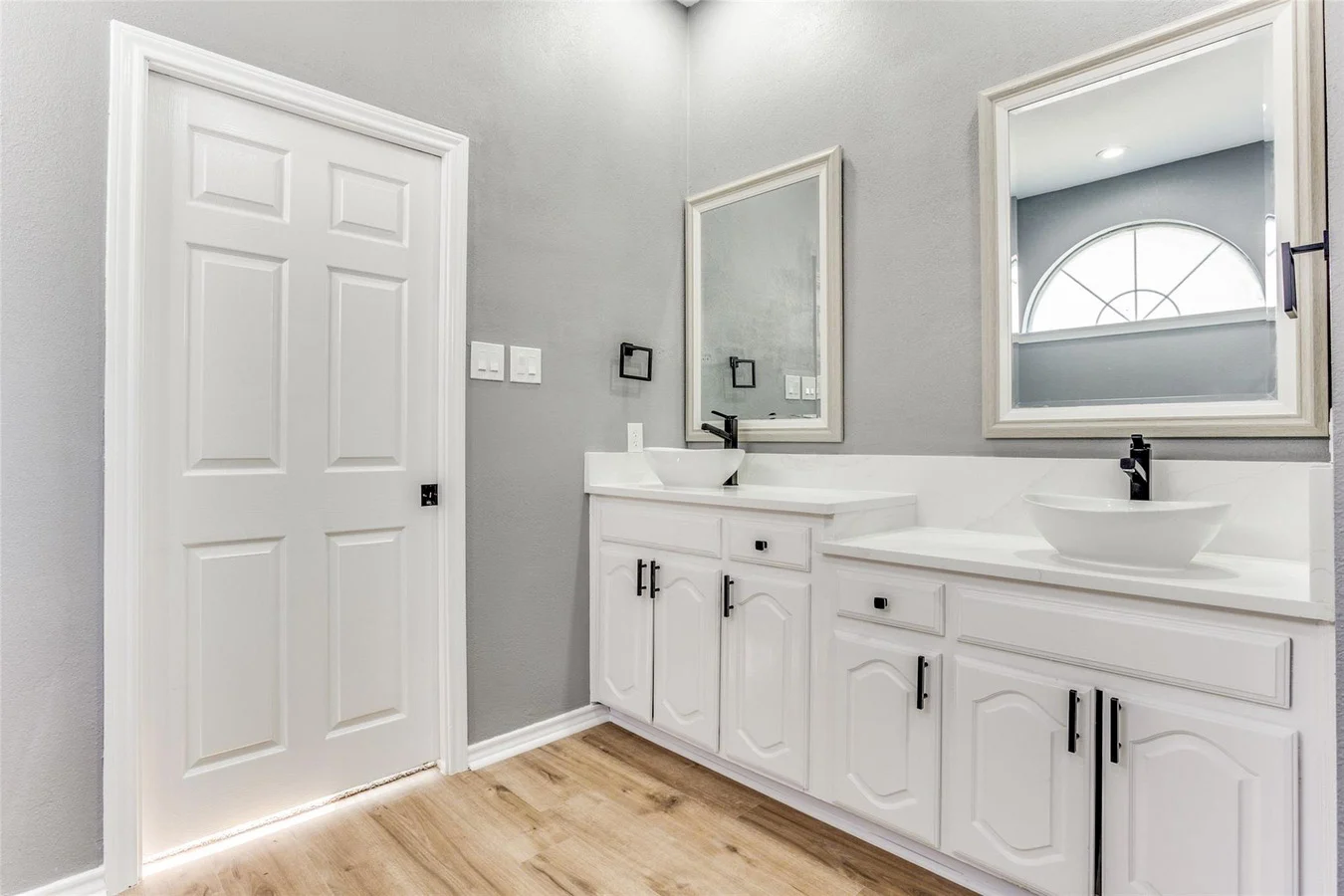 Primary bathroom with a white double vanity, vessel sinks, gray walls, black fixtures, and a large arched window in Rowlett, Texas.