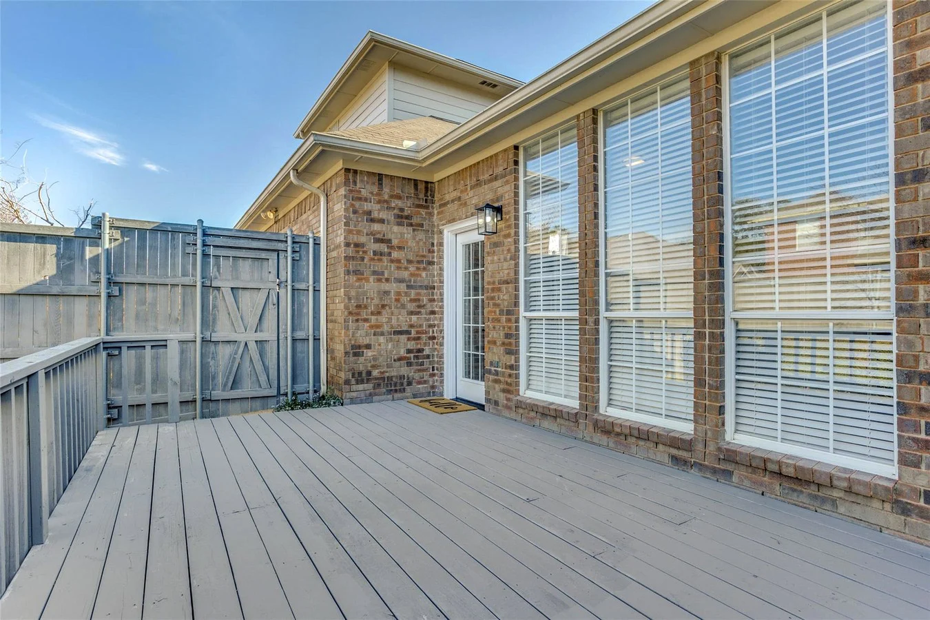 Rear deck beside the brick Rowlett home with broad windows, refreshed exterior surfaces, and fenced outdoor space in Rowlett, Texas.