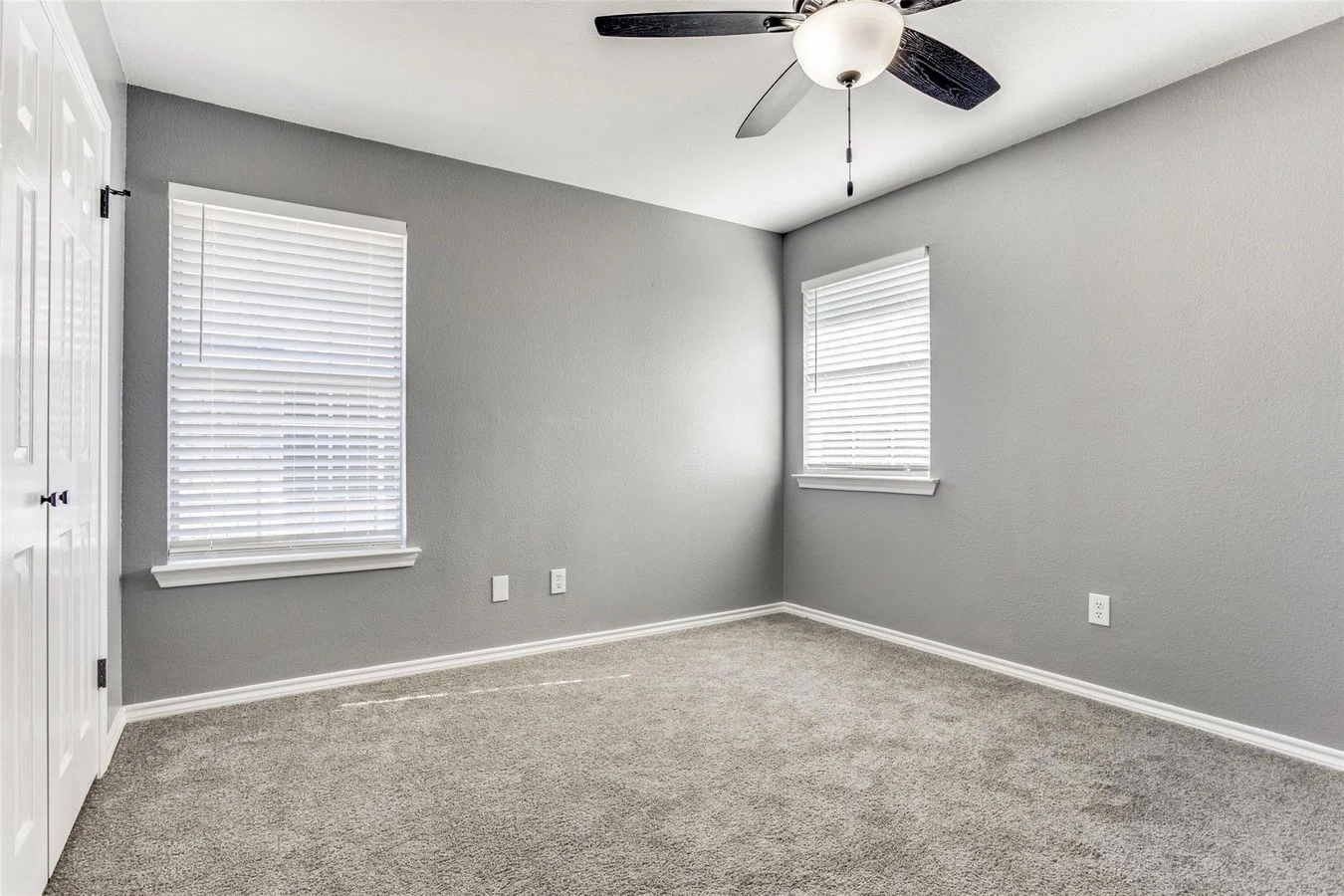 Secondary bedroom with gray carpet, gray walls, white trim, windows on two walls, and a ceiling fan in Rowlett, Texas.