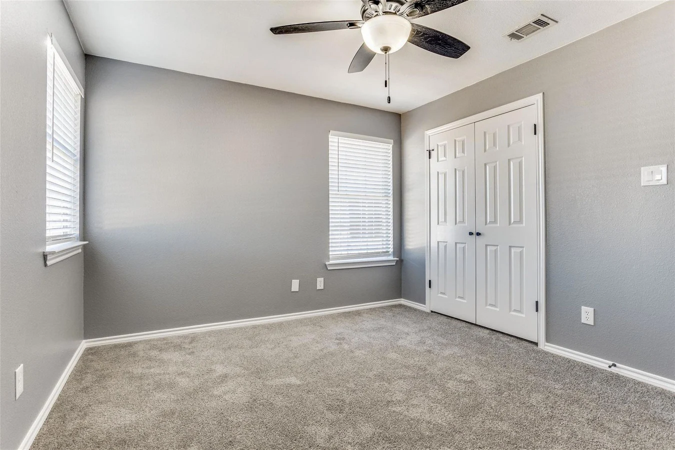 Secondary bedroom with gray carpet, gray walls, white trim, a wide window, double closet doors, and a ceiling fan in Rowlett, Texas.