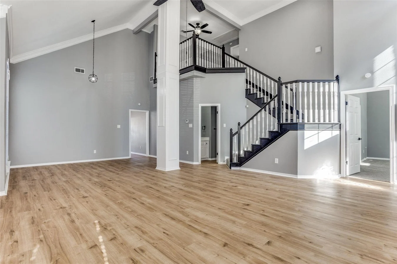 Two-story foyer and open living area with light wood flooring, black stair railings, gray walls, and modern lighting in Rowlett, Texas.