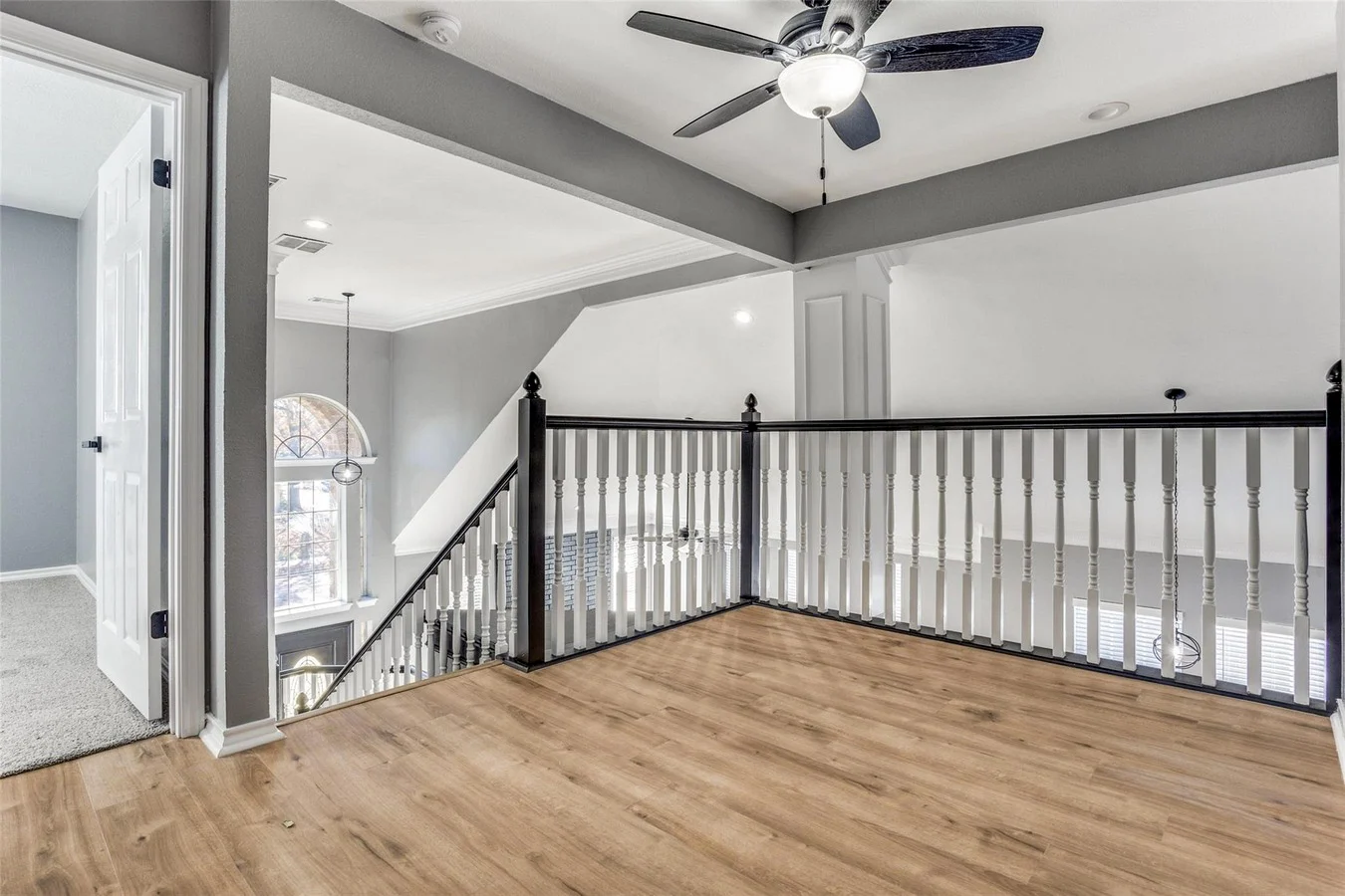 Upper landing with light wood flooring, black stair railing, gray walls, and views into the two-story foyer in Rowlett, Texas.