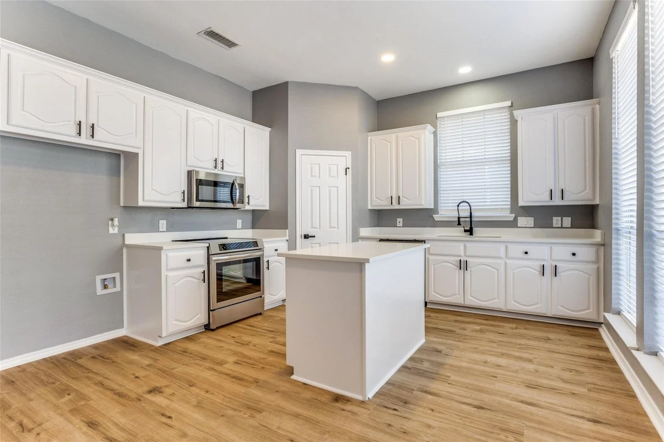 White kitchen with a center island, stainless steel appliances, light wood flooring, recessed lighting, and gray walls in Rowlett, Texas.